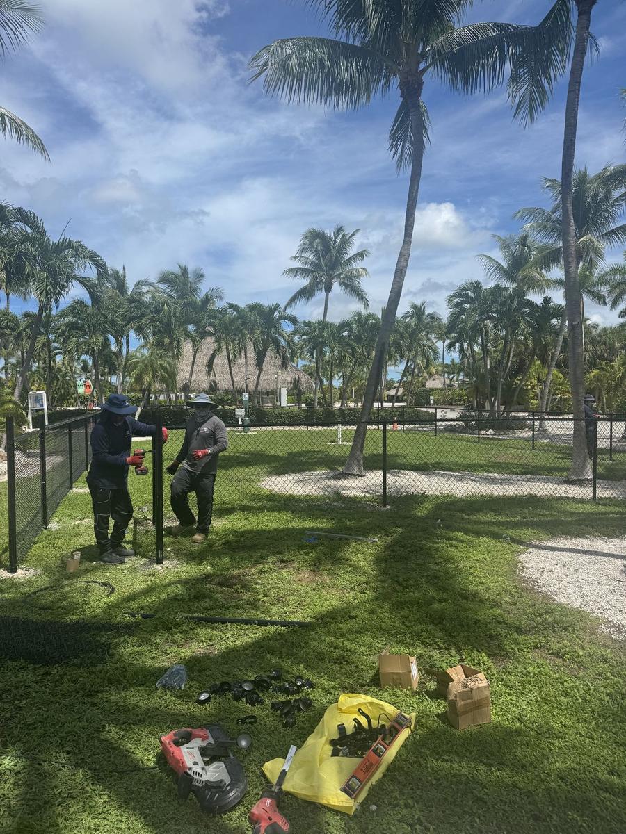 Crew installing black vinyl coated chain link fence at a dog park