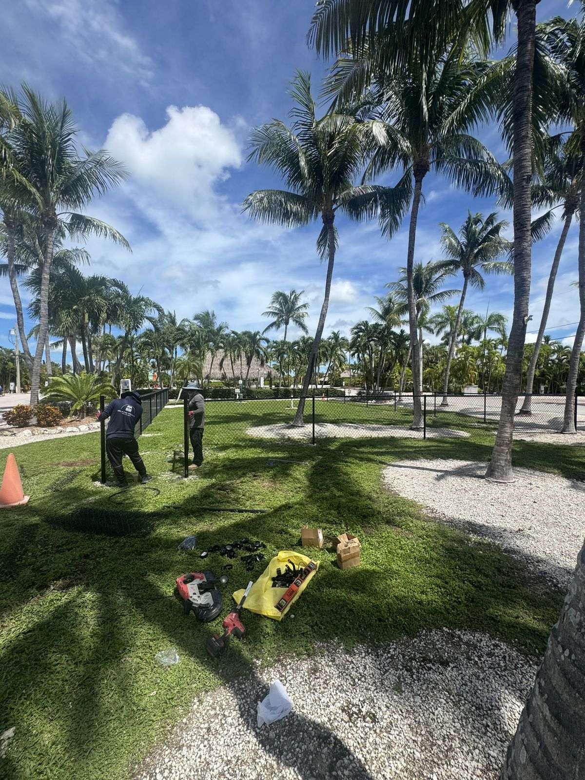 Island Fence crew installing black vinyl coated chain link fence beneath palm trees in the Florida Keys