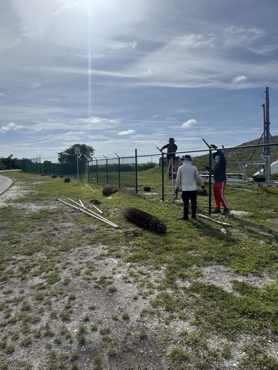 Island Fence crew installing green vinyl coated chain link security fence with barbed wire